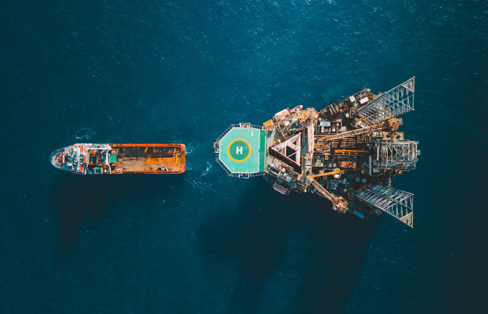 Aerial view of an offshore oil rig with a helipad in the ocean, adjacent to a cargo ship.