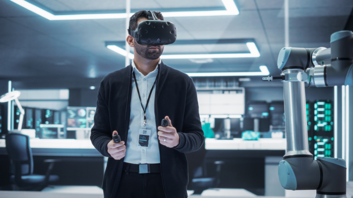 A person wearing a virtual reality headset operates a robotic arm using handheld controllers in a modern, high-tech room.